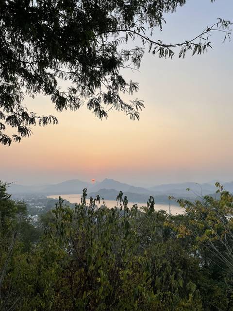 Sunset over distant mountains with trees in the foreground.