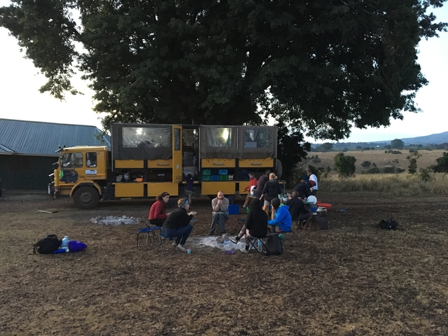 Group of people camping with a large vehicle in a rural setting.