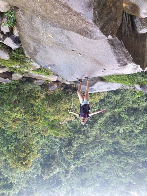 A person posing with arms open on a rock in a forest area.