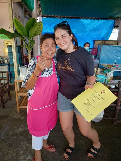 Person smiling with another individual holding a book, likely in a cooking class setting.