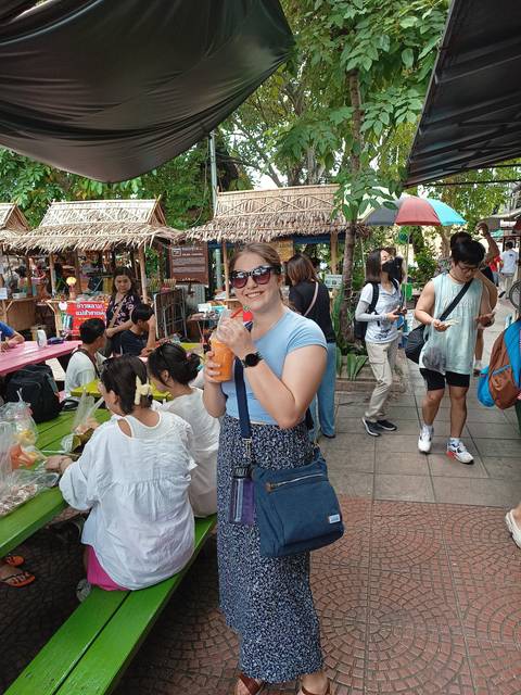 Market scene with a person holding a smoothie, others enjoying local food.