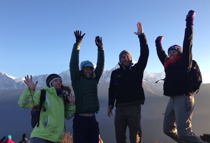 Group of people in winter attire, raising hands joyfully with snowy mountain backdrop.
