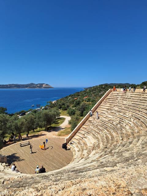 Ancient amphitheater by the sea with people exploring.
