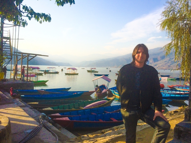 Person posing by colorful boats at a lakeside.