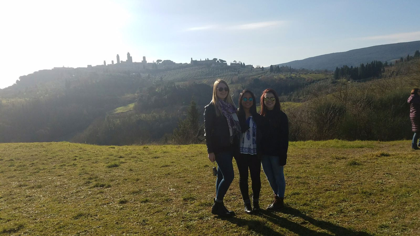 Three people posing on a grassy hill with a skyline in the background.