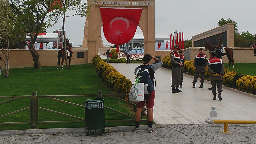 A person standing before a Turkish national monument with guards visible.