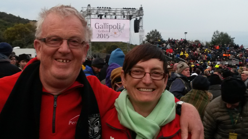 People gathered outdoors for an event with a prominent sign in the background.