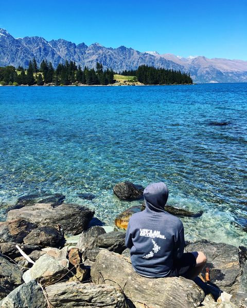 Person sitting on a rocky shore with clear water.