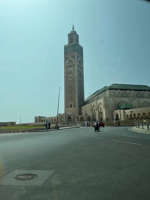 Tall mosque minaret viewed from the street with traffic and people.