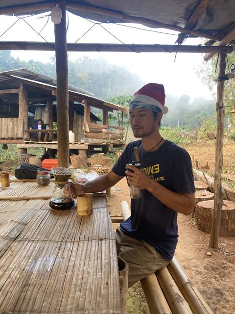 Person wearing a Santa hat holding a beverage on a rustic table outdoors.