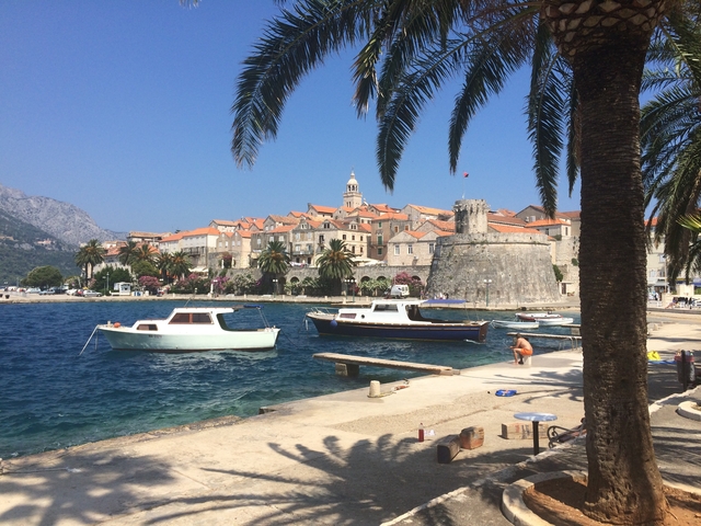       Coastal town with fortification and boats docked along the water.
  