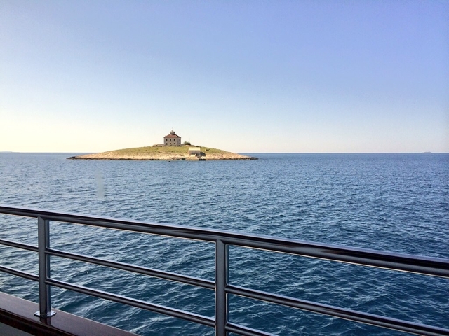       Lighthouse on a small island, viewed from a boat on the sea.
  
