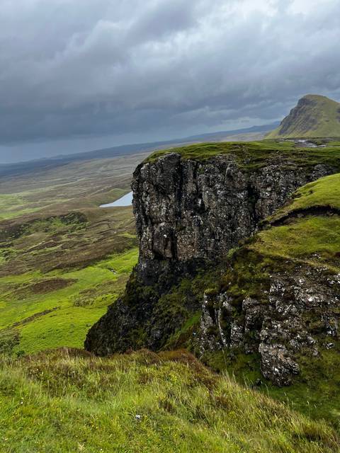 Rocky landscape with green vegetation and cloudy sky.