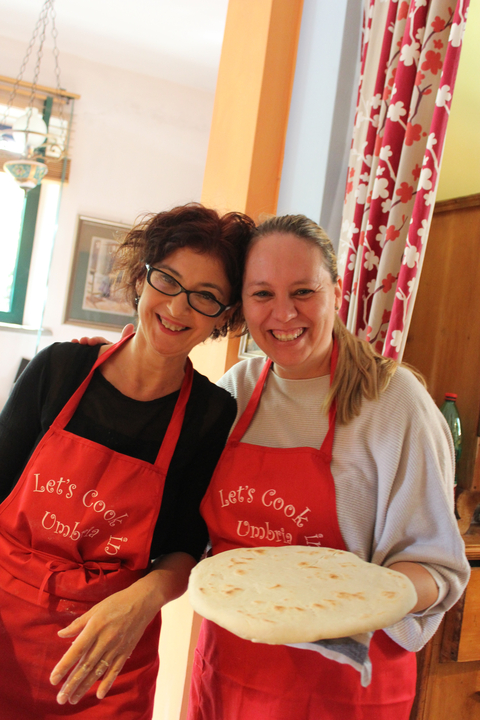 Two women smiling, wearing cooking aprons.