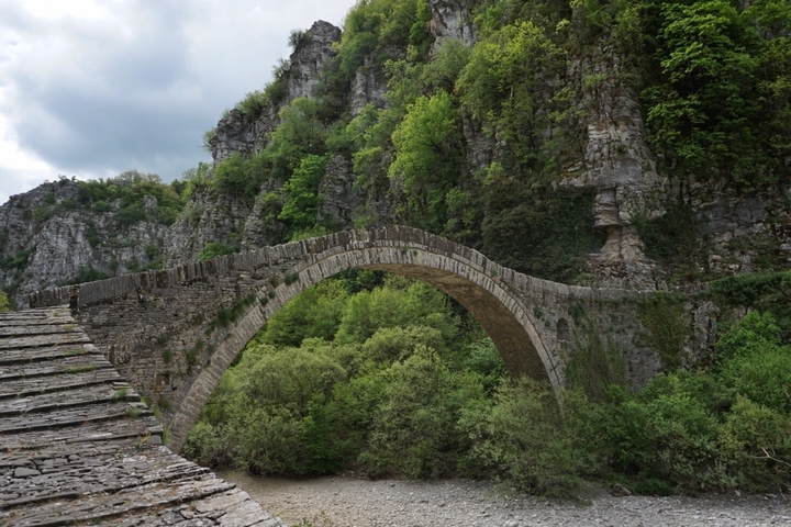       An ancient stone bridge over a lush green gorge.
  