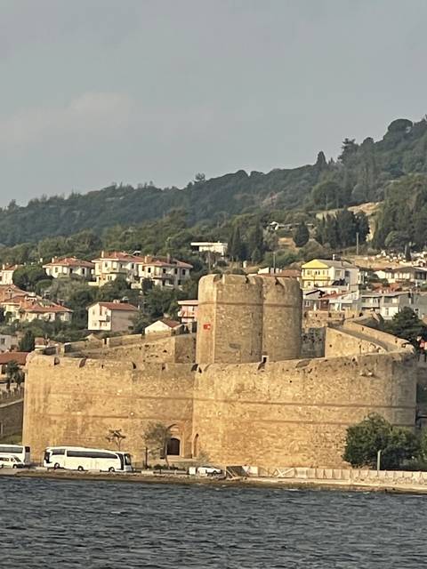       Seaside fortress with buildings and a Turkish flag.
  