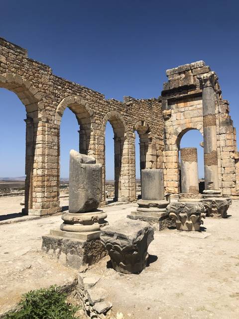       Ancient ruins with stone arches and pillars under blue sky.
  