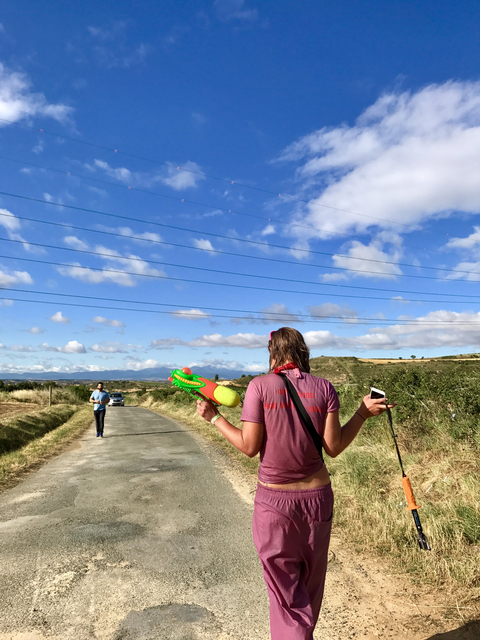       Person with a water gun on a rural road under a blue sky.
  