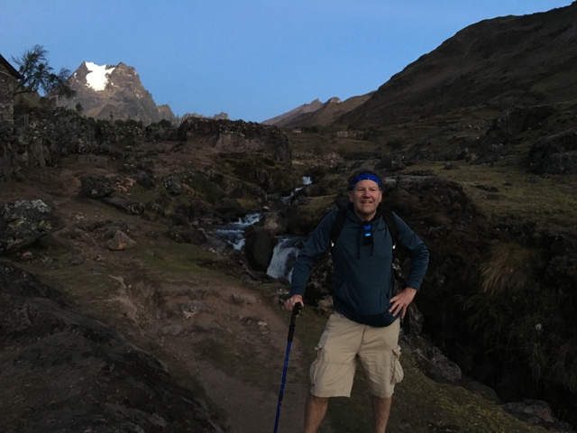 Man posing on a scenic mountain trail with a waterfall.