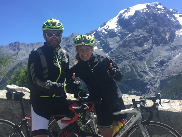 Cyclists posing with thumbs up, snow-capped mountains in the background.
