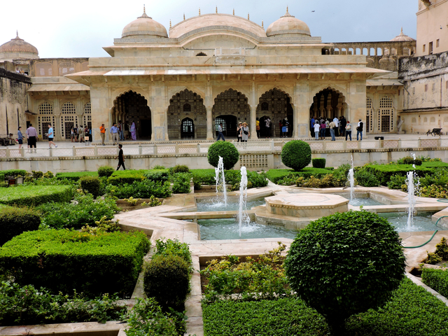       A historical building with fountains and gardens in front.
  