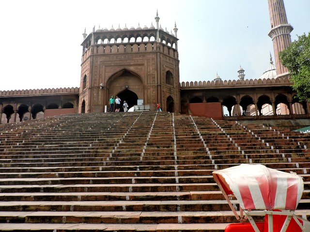       A red fort entrance with wide stairs and people climbing.
  