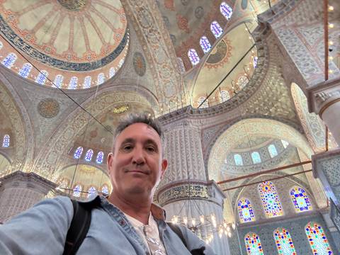       Interior view of a large ornate mosque with a visitor in the foreground.
  