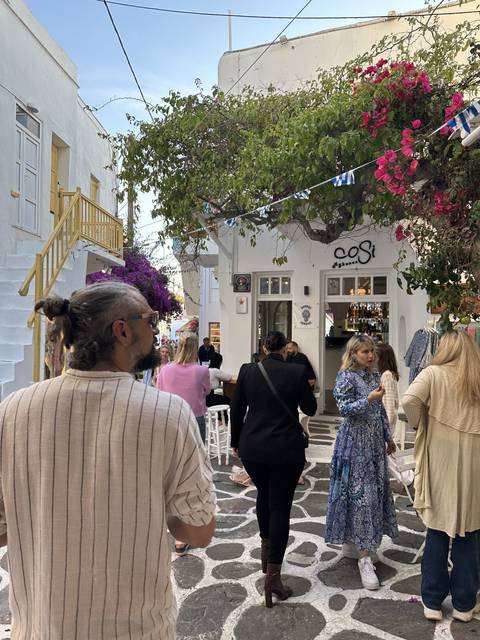 People walking on a quaint narrow street with cafes and flowers.