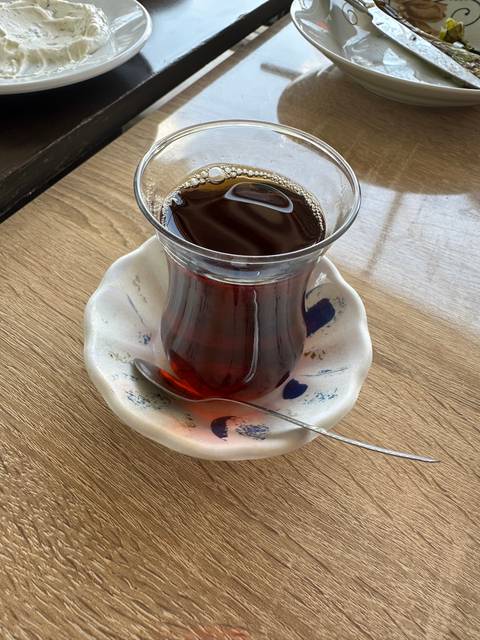       Glass of tea on a saucer placed on a wooden table.
  