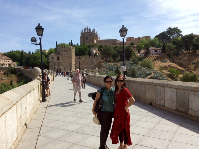 People standing on a stone bridge with a historic city in the background.