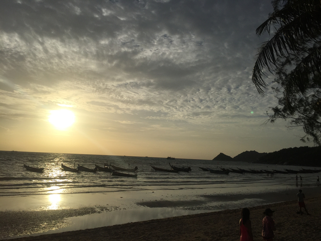 Sunset on a beach with longtail boats in the water.