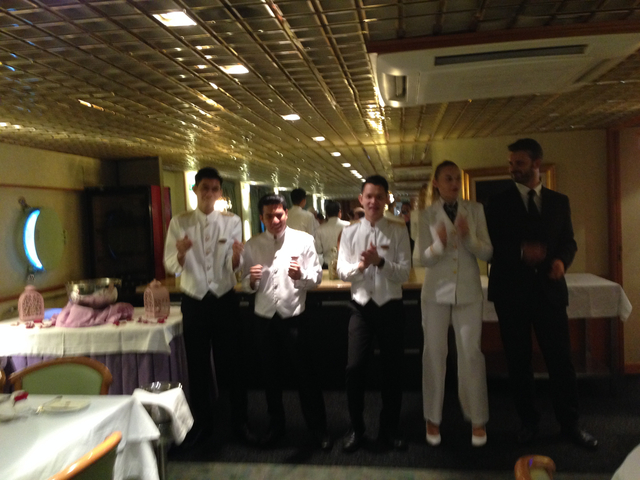A group of waitstaff in formal attire poses inside a dimly lit restaurant.
