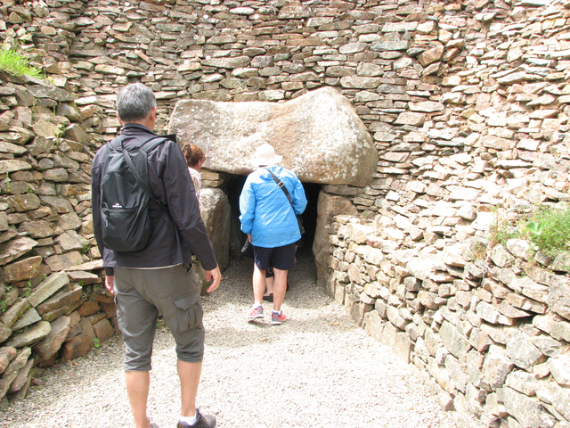 People entering a prehistoric stone structure surrounded by rock walls.
