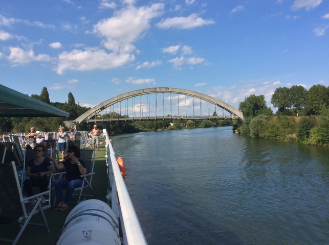 A riverboat with people passing under a large bridge.