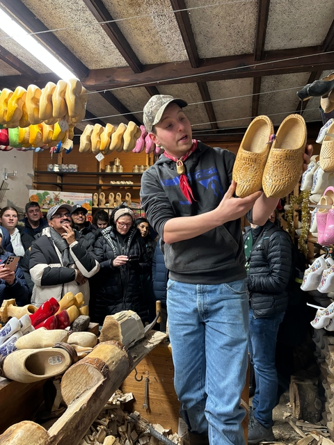 A group of people inside a shop, watching a demonstration of wooden shoes.