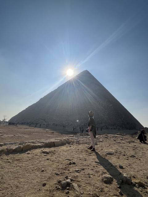       Man walking near pyramids with the sun low in the sky.
  