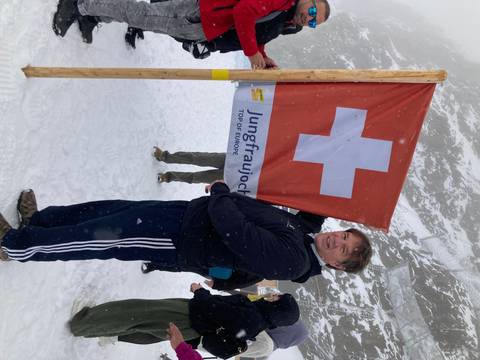 Person holding a Swiss flag on a snowy mountain.