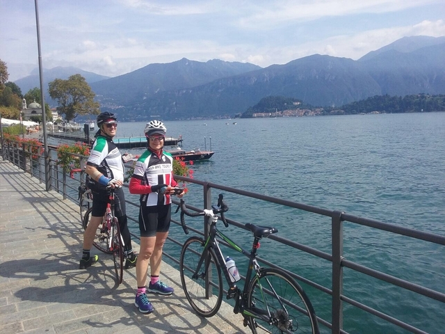Two cyclists posing by a lake with mountains in the background.
