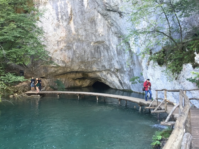       People walking across a wooden bridge over a waterway leading into a cave.
  