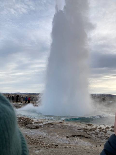       A geyser erupting with steam and people nearby.
  