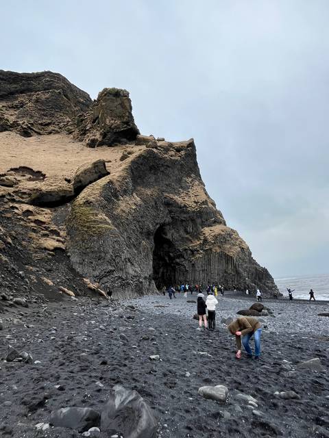       A rocky beach with unique basalt columns and visitors.
  