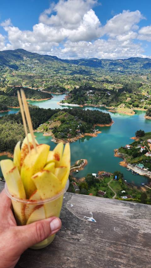       Scenic view of a lake with a hand holding fruit in the foreground.
  