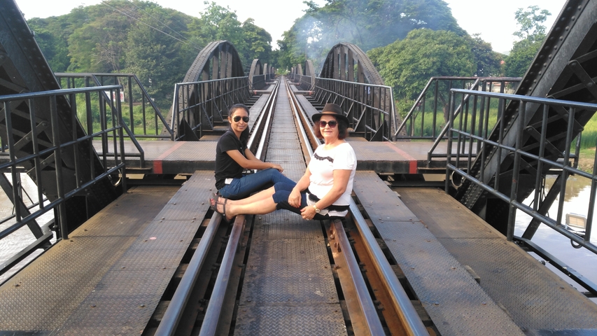 Two women sitting on railway tracks of a historic bridge.