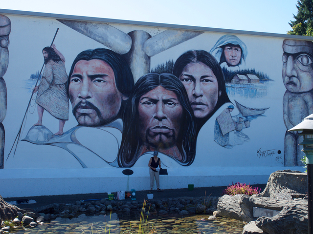 Large mural with indigenous faces and painter at work.