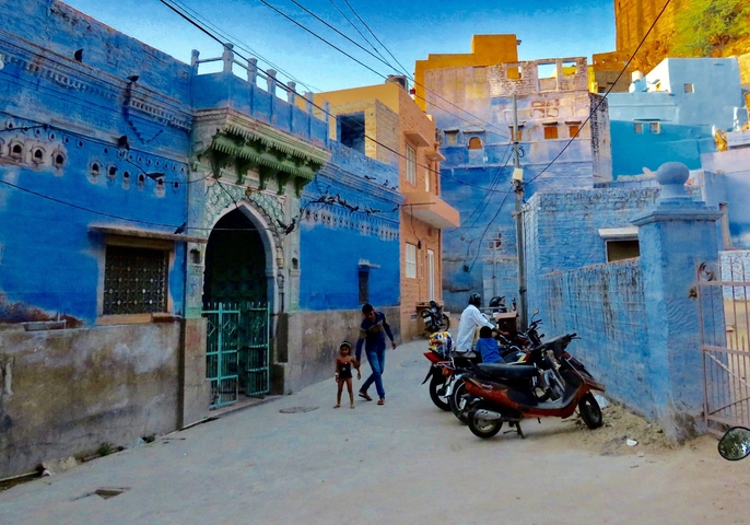 Vibrant blue buildings on a street with scooters.