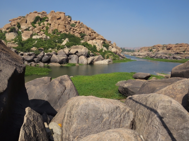       Stone boulders surrounding a tranquil riverbed with greenery.
  