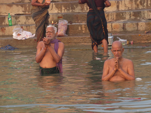       Two men performing religious rituals in a river.
  
