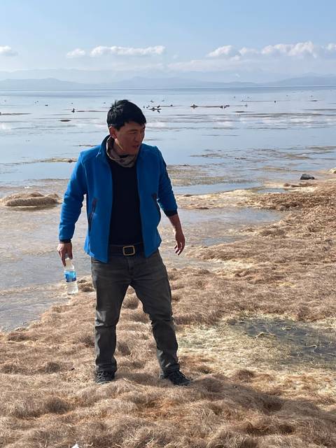 A person standing on dry grass near a body of water.