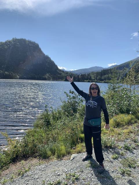       Person posing by a lake with mountains in the background.
  