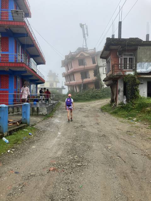       Hiker walking through a foggy rural road with buildings.
  